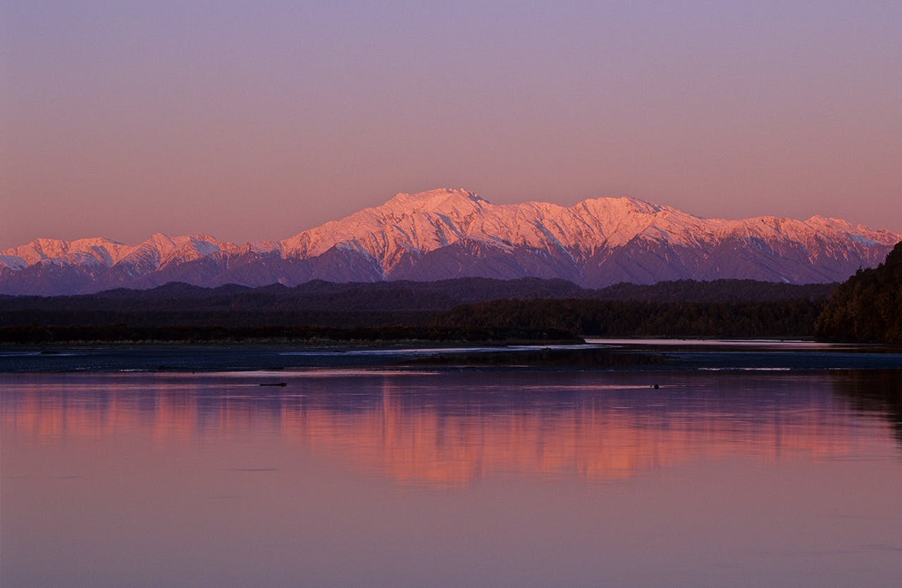 The Southern Alps tower over a mirror-calm Okarito Lagoon. Photo: Steve Baker/Black Robin Photography